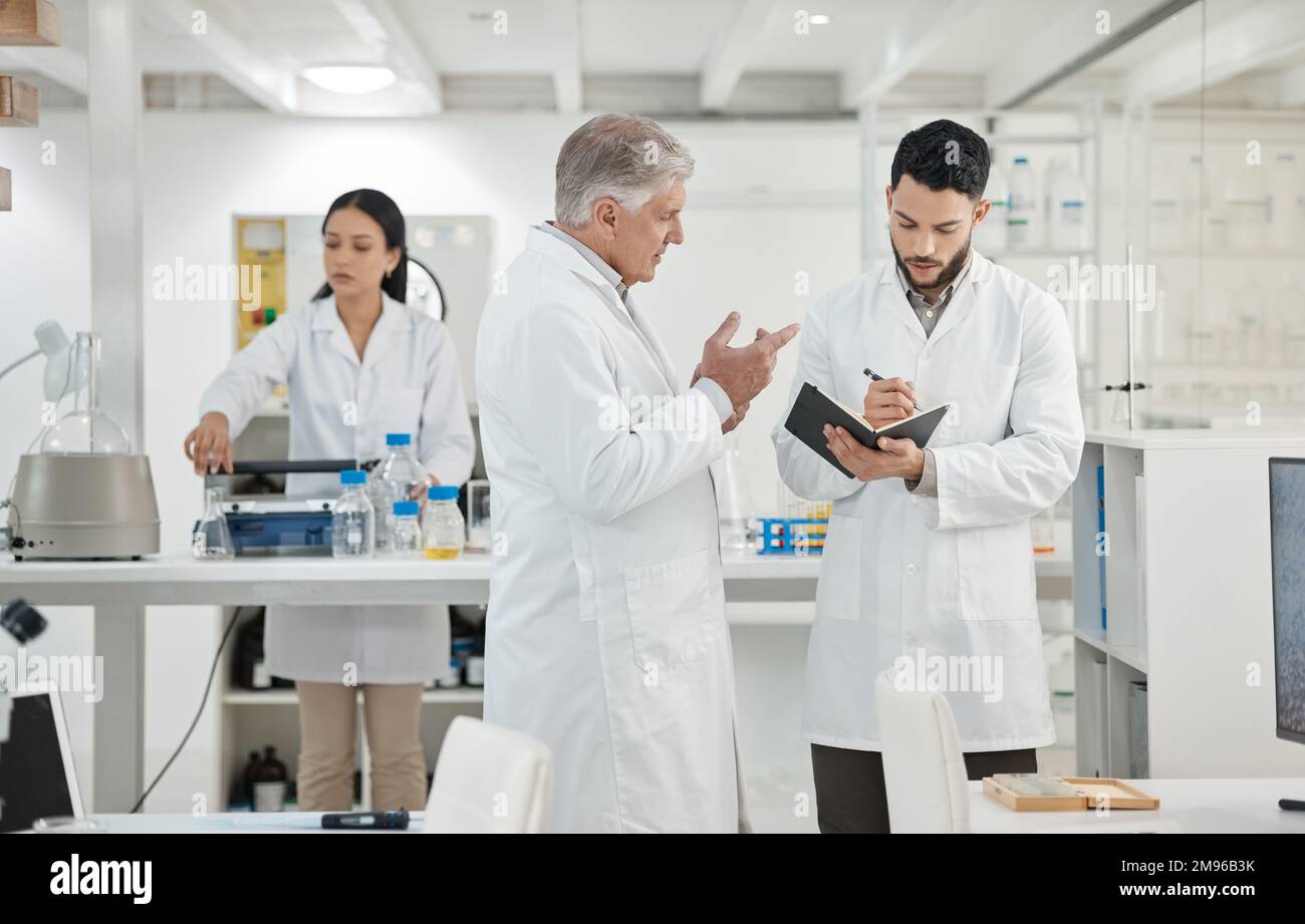 Id like you to set up the next experiment on your own. two scientists writing notes while having a discussion in a lab. Stock Photo