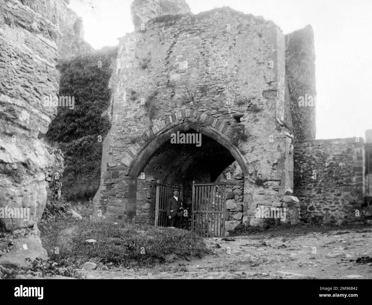 The wide gothic-style entrance to the medieval Bishop's Palace, with a man standing at the open gate, in St David's, Pembrokeshire, Dyfed, South Wales.  Some parts of the building date from the 12th century, but most of the work was done in the 14th century. Stock Photo