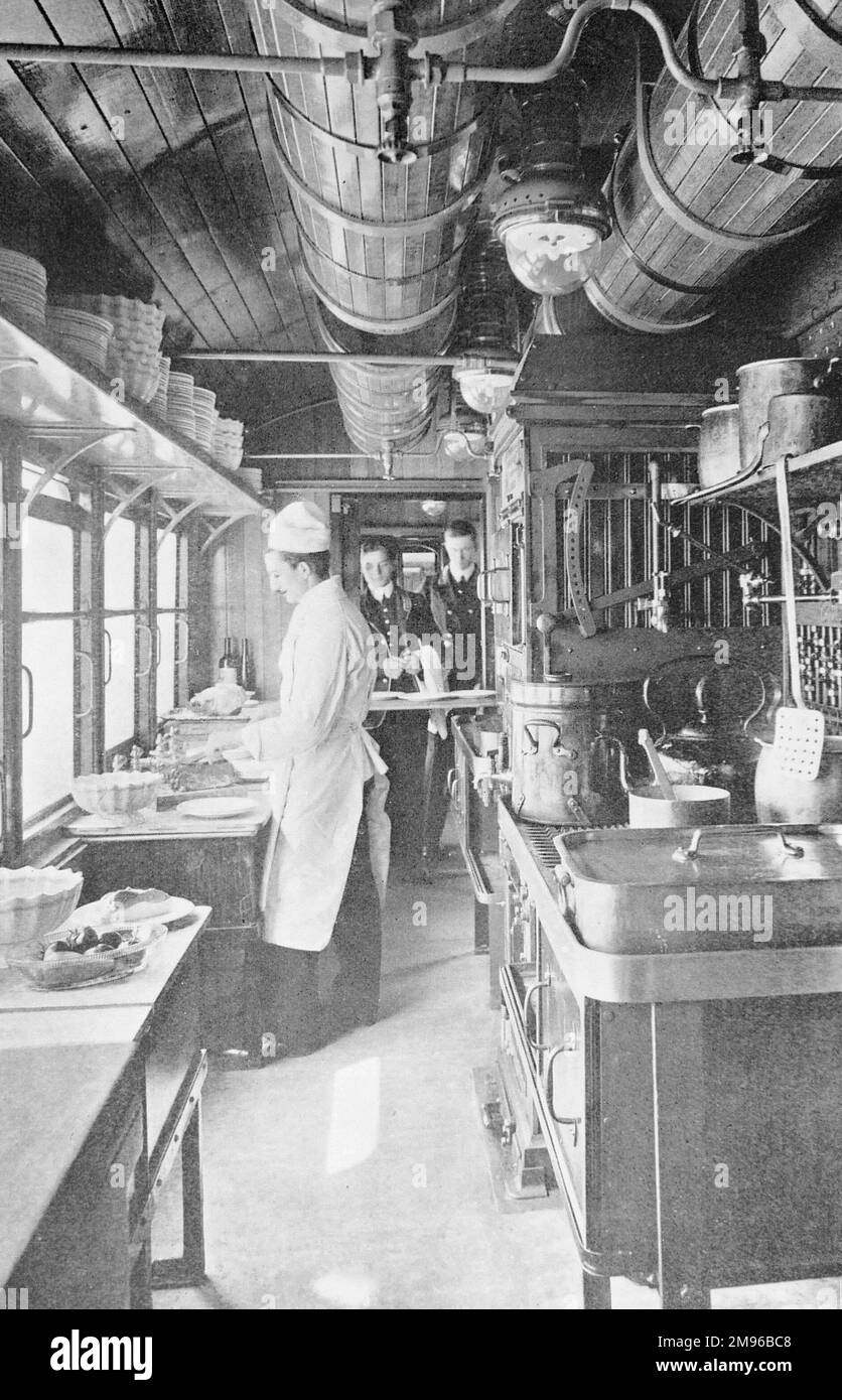 View inside a galley kitchen on an LNWR (London and North Western Railway) restaurant car, with a chef at work and two uniformed waiters waiting to serve food to their customers. Stock Photo