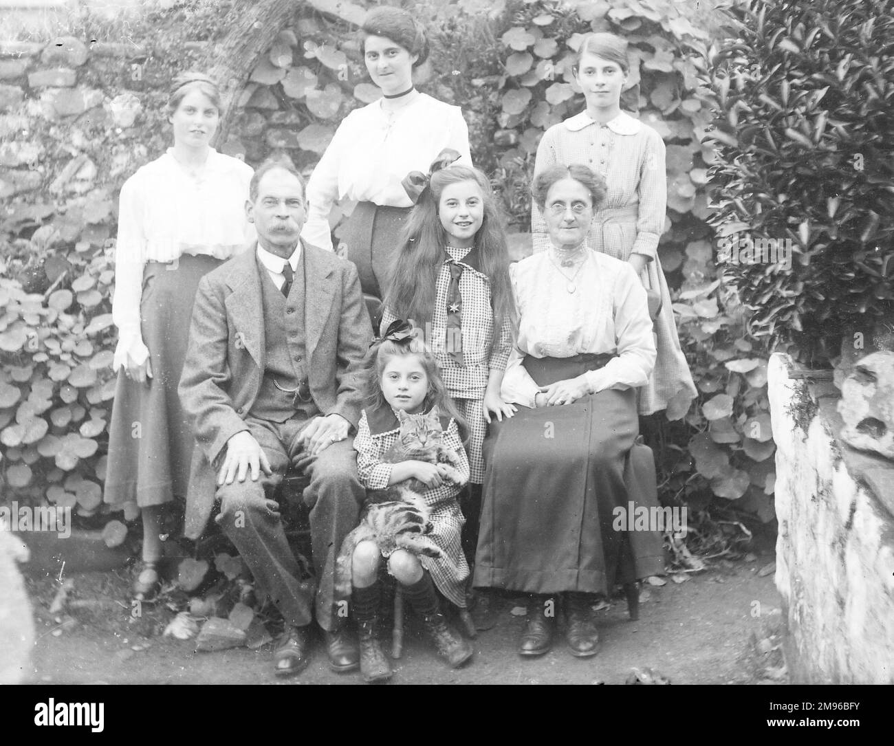 A middle class Edwardian family  pose for a group photograph in a garden, probably in the Mid Wales area.  The little girl in the middle is holding a tabby cat in her arms. Stock Photo