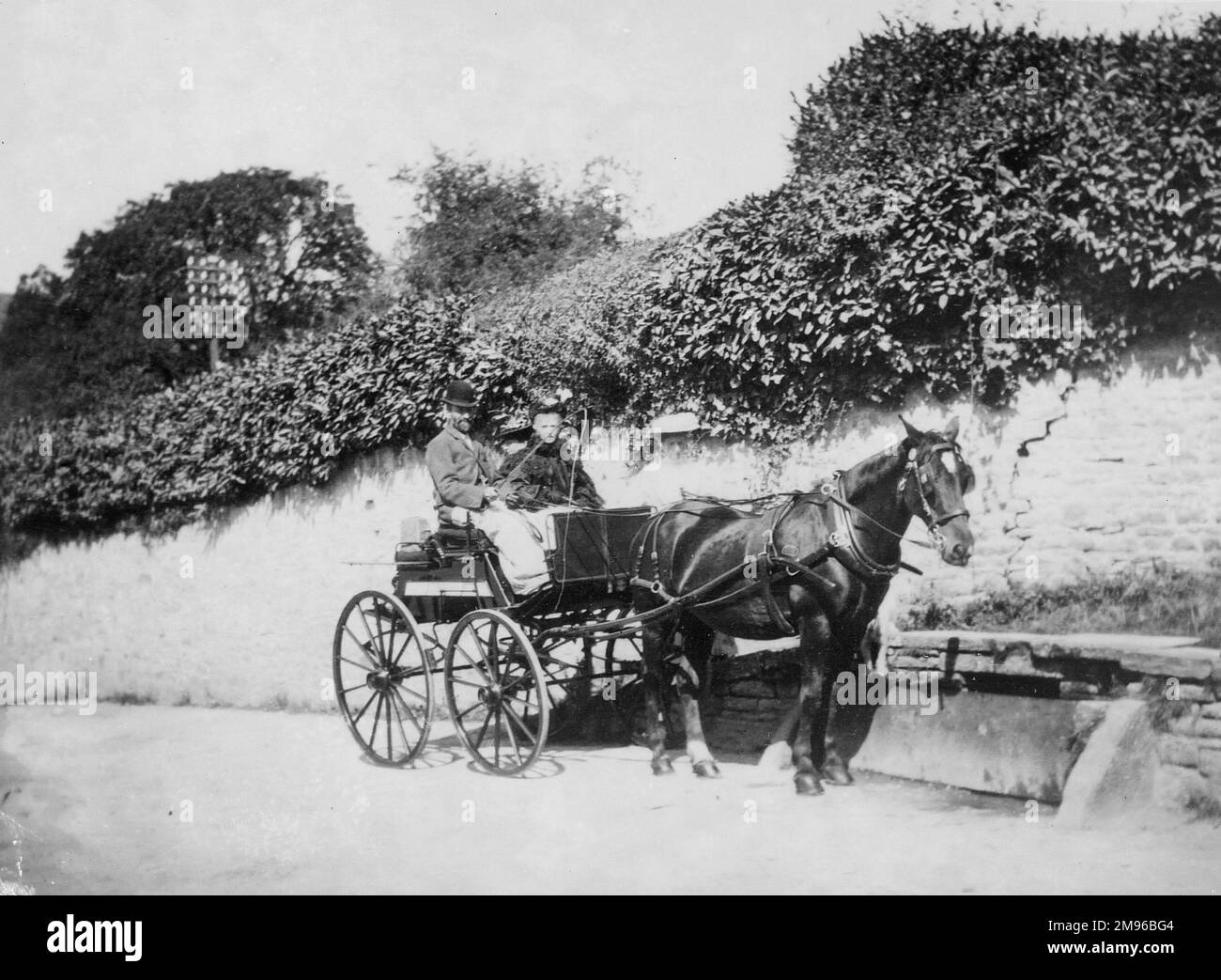 A horse drawn trap with two passengers outside Crickhowell Castle wall
