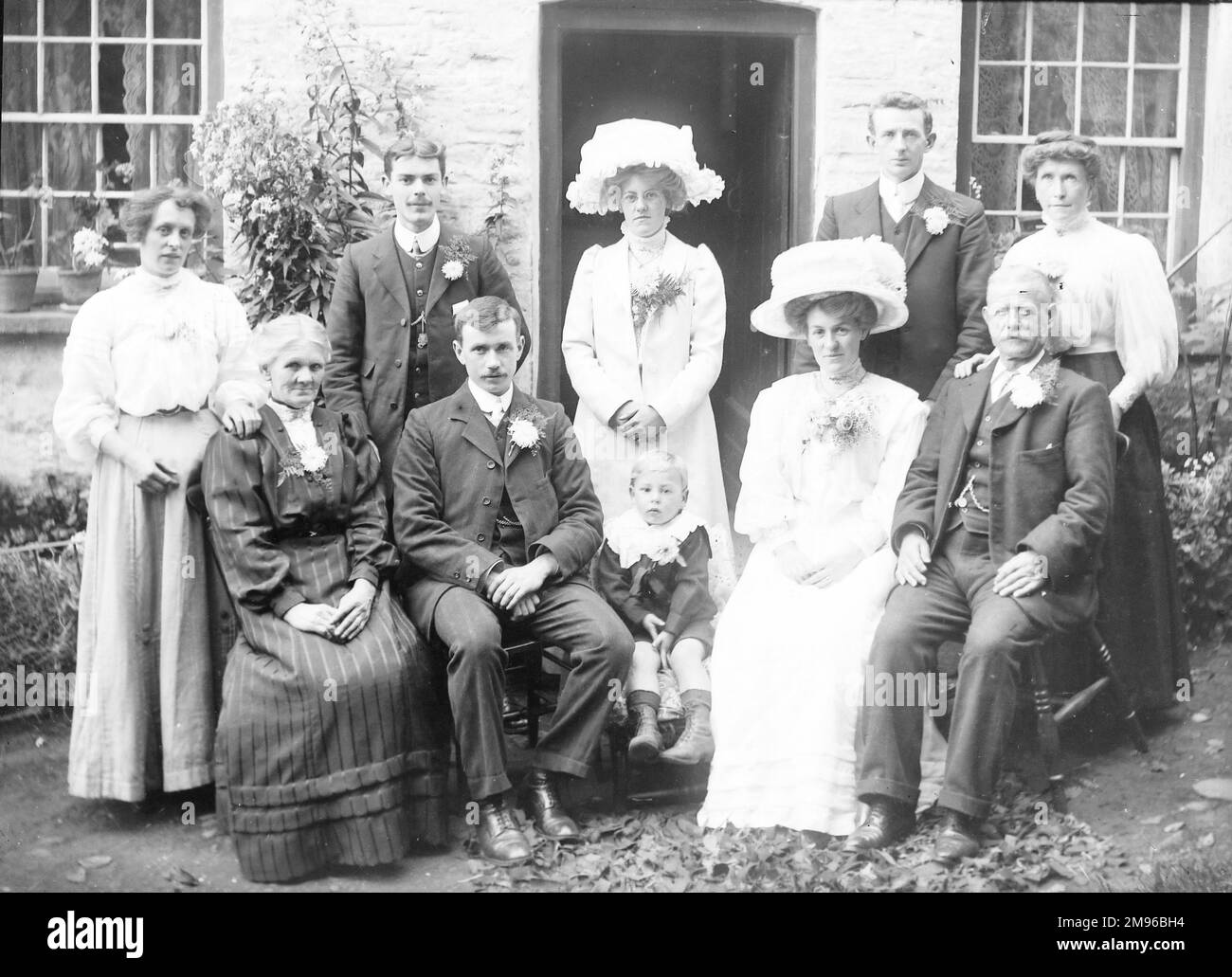 A middle class Edwardian family in their best clothes, pose for a group photograph outside their house, probably in the Mid Wales area.  There are five women, four men, and a child.  Two of the women are wearing enormous hats.  The men are wearing flowers in their buttonholes -- perhaps they have all been to a wedding. Stock Photo