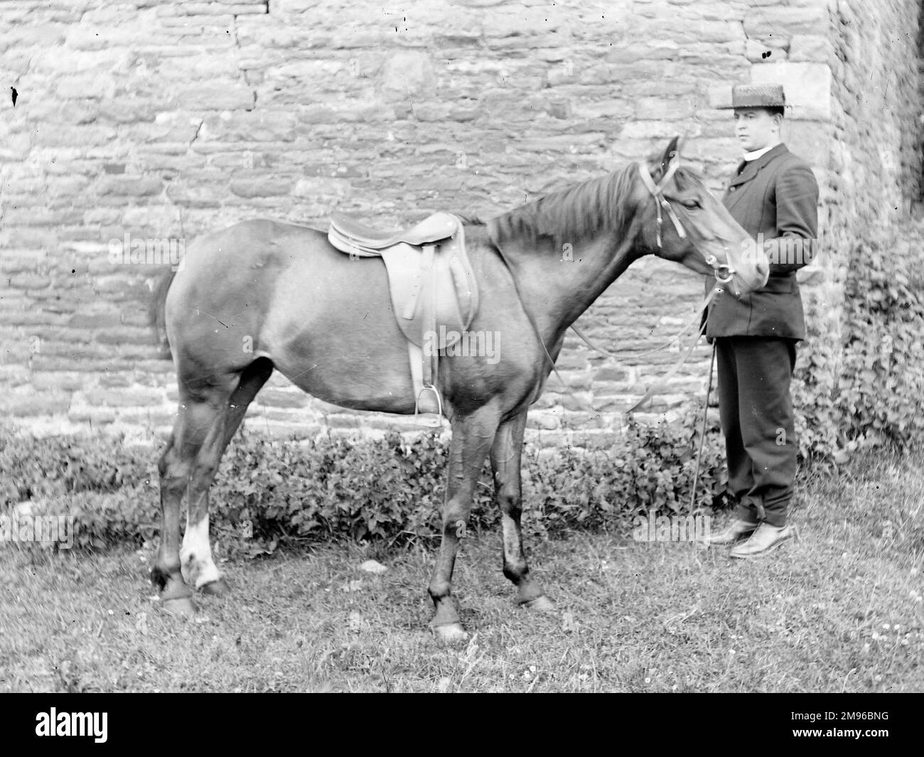 A vicar and his horse in front of a stone wall, probably somewhere in