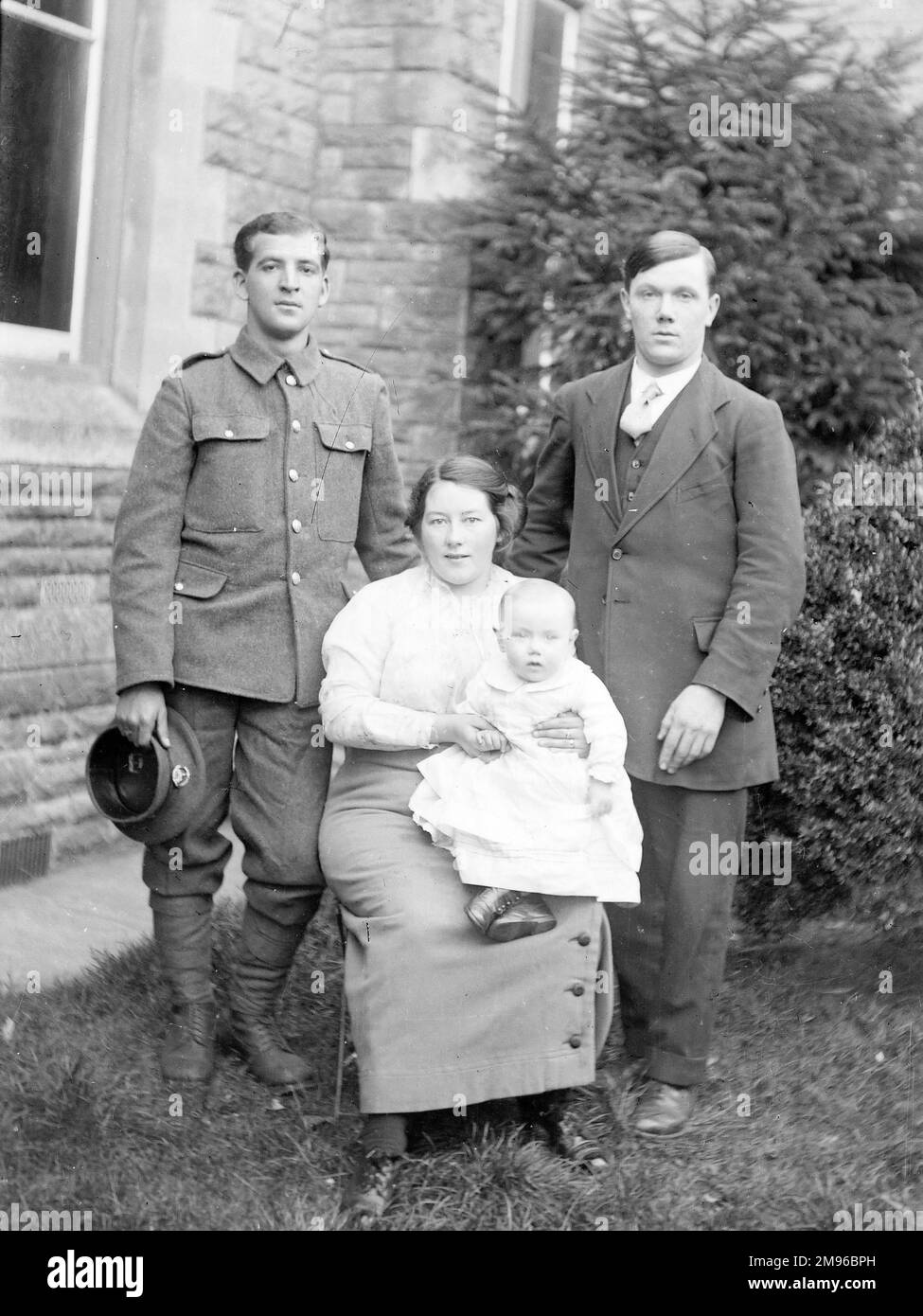 A family group photo in a garden, with a mother, her baby, and two men, one of them in uniform, during the First World War. Stock Photo