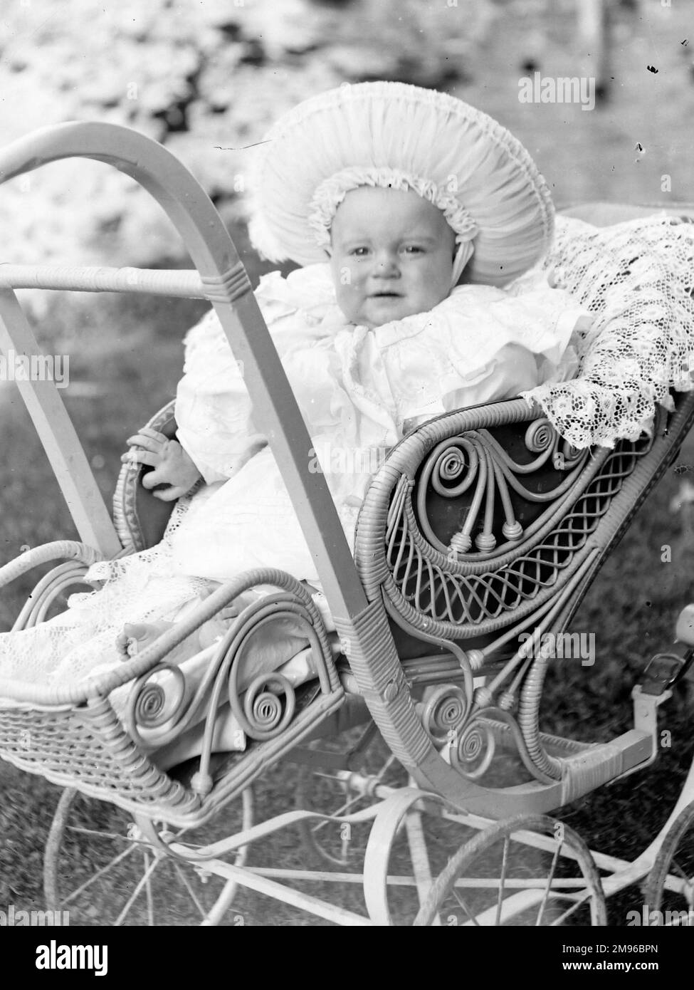 An overdressed baby in an ornate pram, in a garden in Mid Wales. Stock Photo