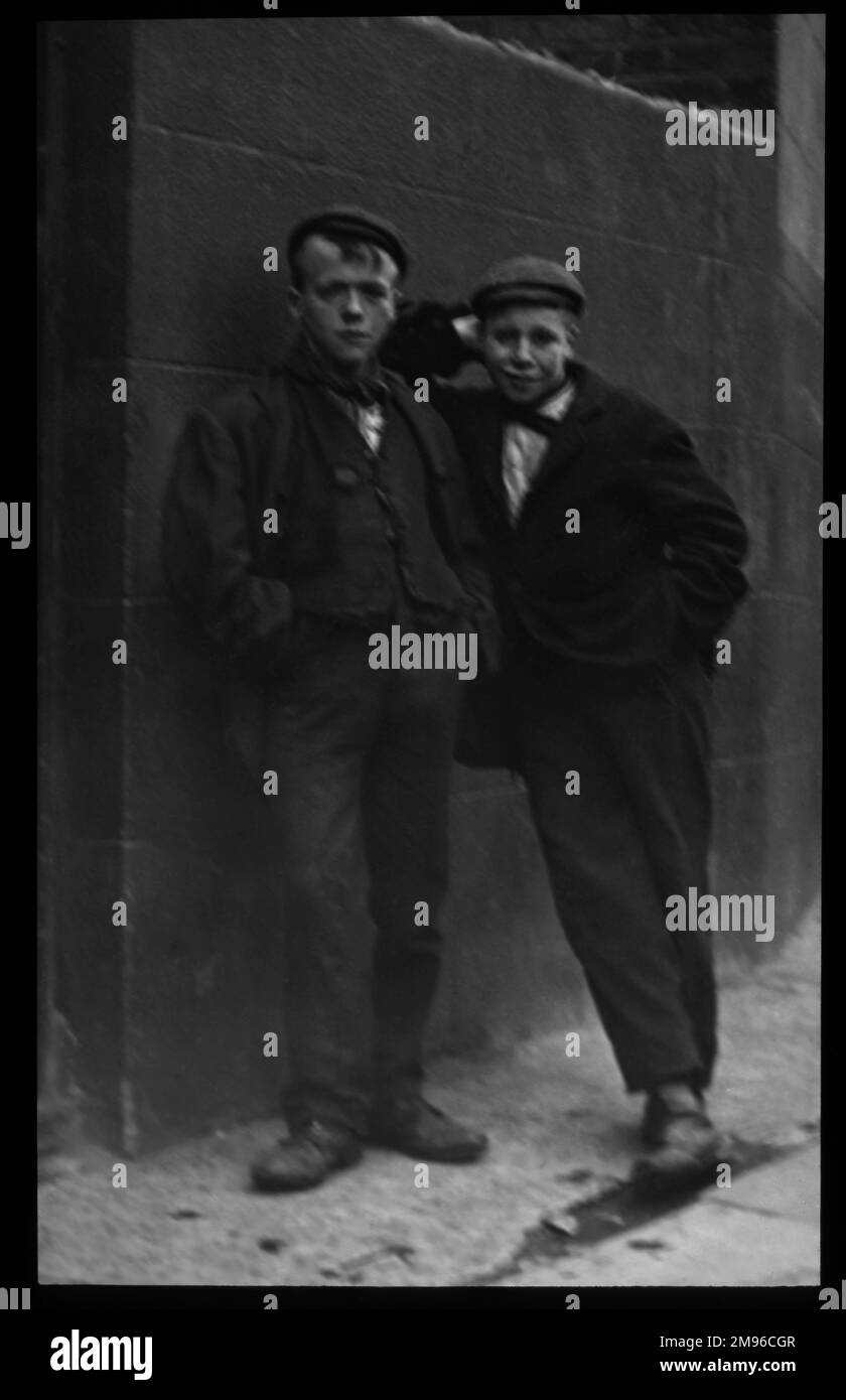Two working class Edwardian boys leaning against a wall on a London
