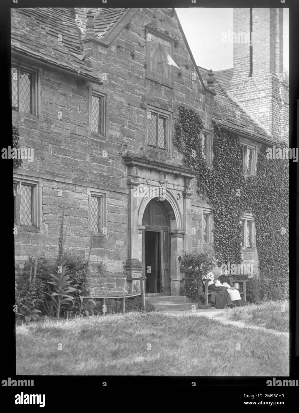 Exterior view of Sackville College, East Grinstead, West Sussex, a Jacobean almshouse founded in 1609 to provide sheltered accommodation for the elderly.  Two elderly women can be seen sitting on a bench to the right of the doorway. Stock Photo
