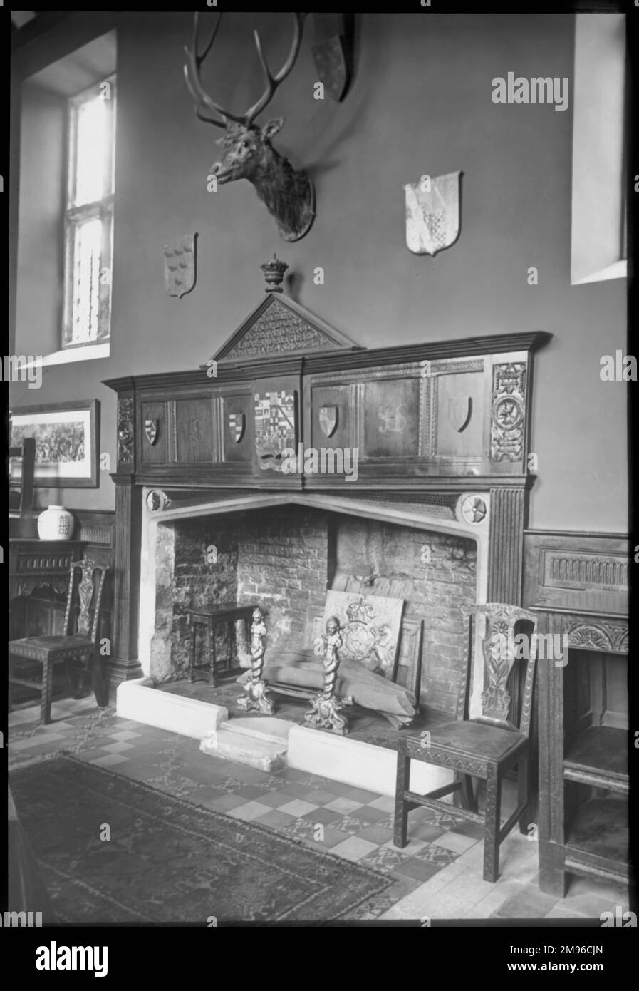 Interior view of the hall of Sackville College, East Grinstead, West Sussex, a Jacobean almshouse founded in 1609 to provide sheltered accommodation for the elderly.  Seen here is a large brick fireplace and grate, with a wooden chair on either side, and a stag's head with antlers above. Stock Photo