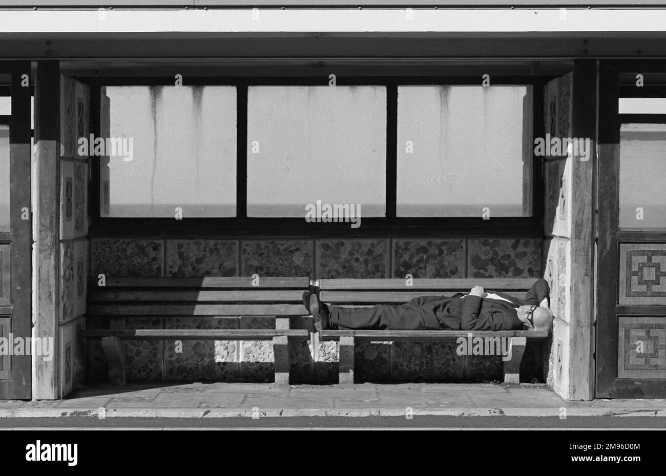 A man asleep on a bench inside a seaside shelter. Stock Photo