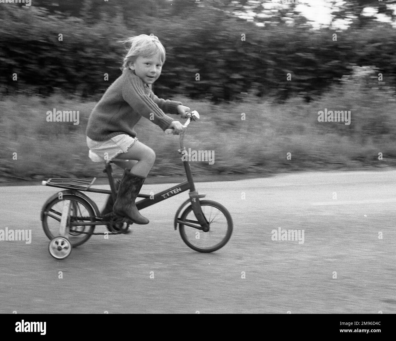 A little boy riding a bicycle with stabilisers on it. Stock Photo
