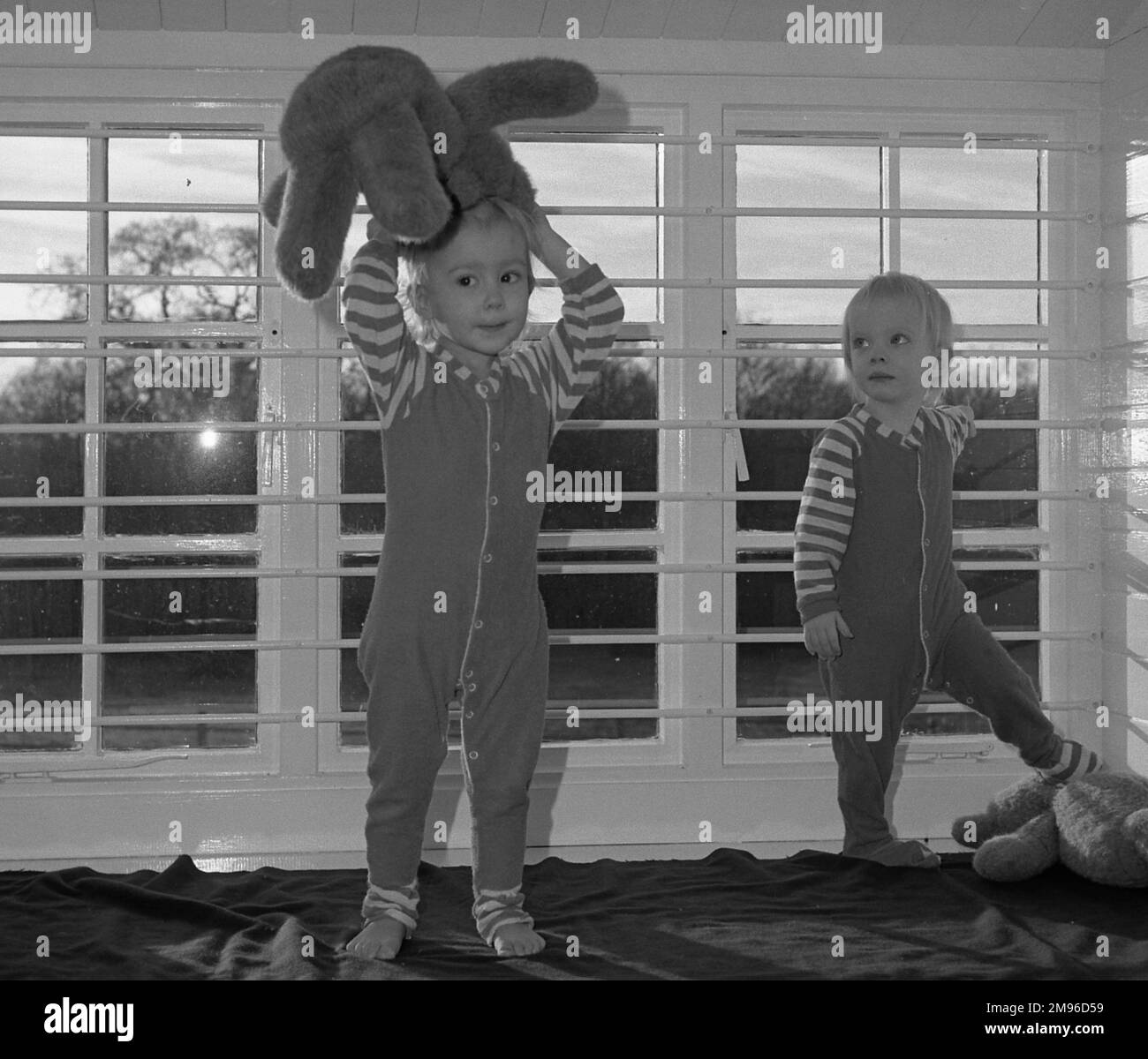 Two small children with their teddy bears in a nursery, standing in
