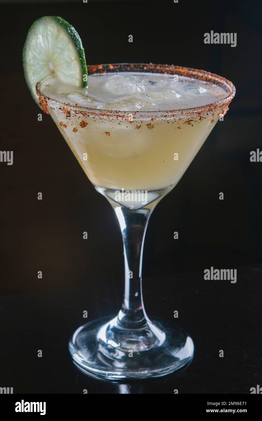 Margarita with lime garnish and tajin rim against a black seamless