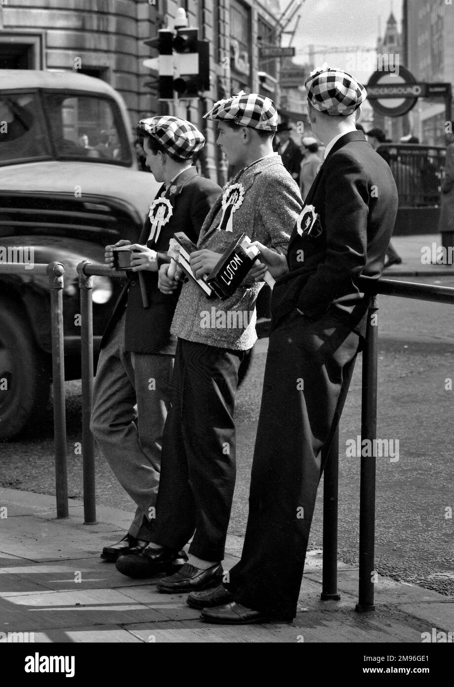 Three football supporters on a London street, wearing checked caps and rosettes and holding rattles. Stock Photo
