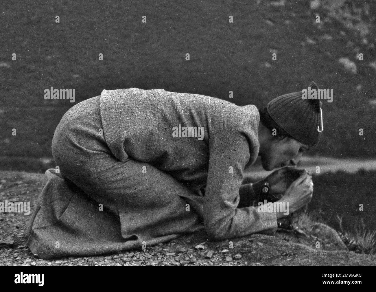 A woman kneeling on the ground, focusing on something.  She is either trying to light a fire, or lining up a camera shot. Stock Photo