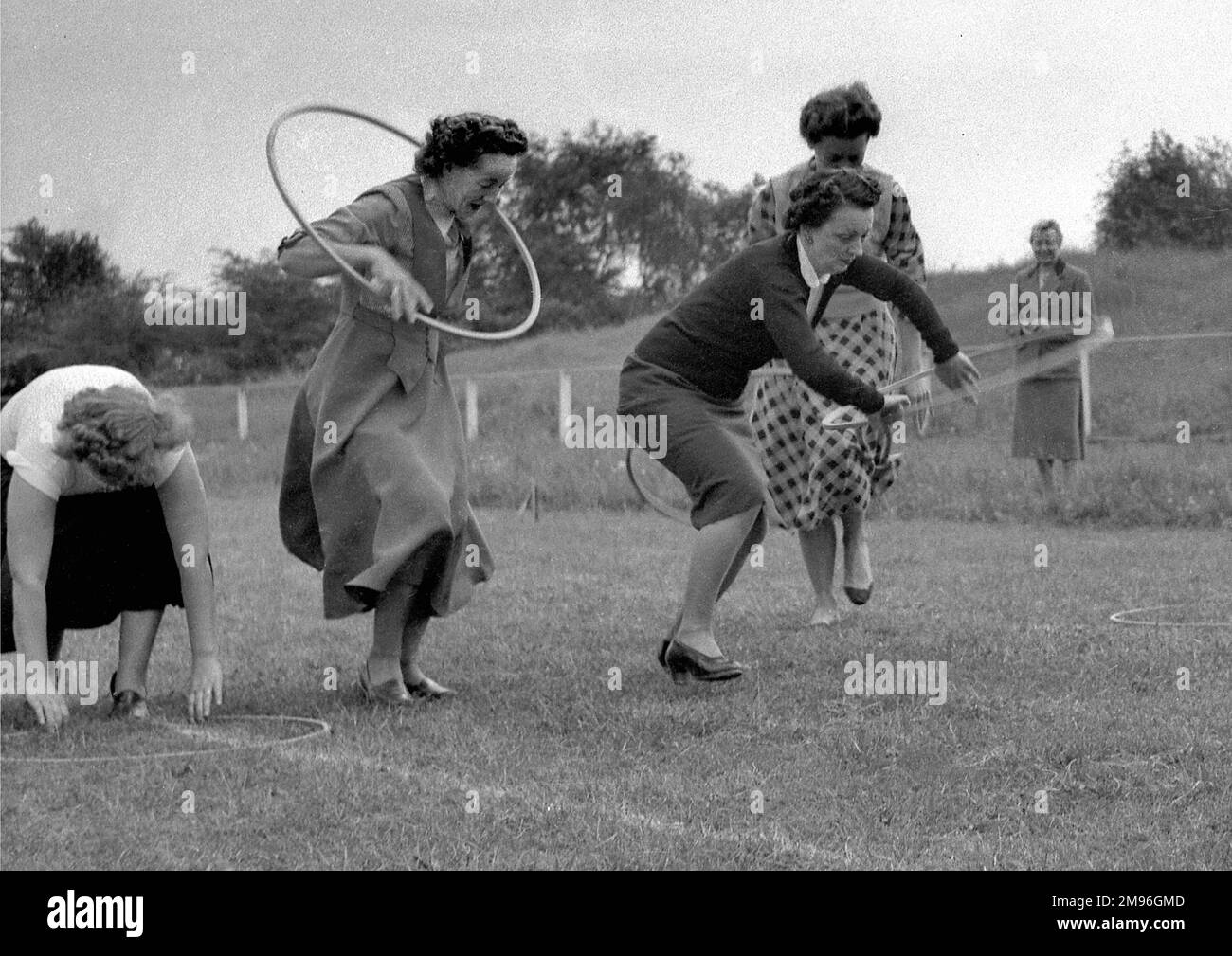 Four women running a race with hoops. A spectator watches, smiling