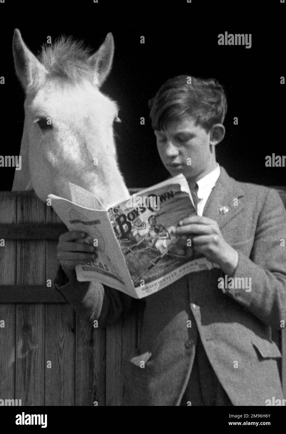 A boy stands reading his Boy's Own magazine, while a white horse appears to be reading over his shoulder. Stock Photo