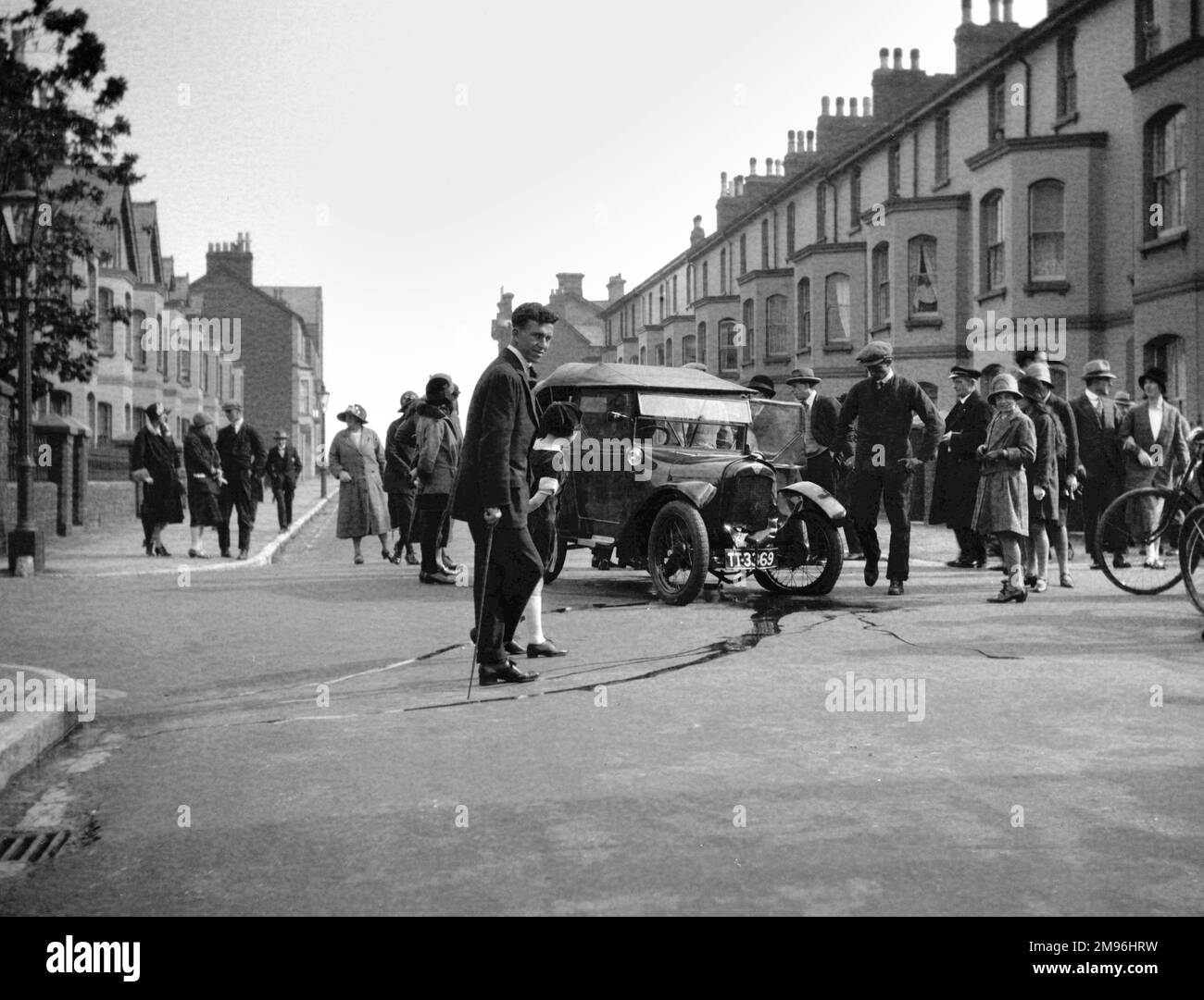Street scene with people gathered round a damaged car.  Water from the broken radiator appears to be running into the gutter. Stock Photo