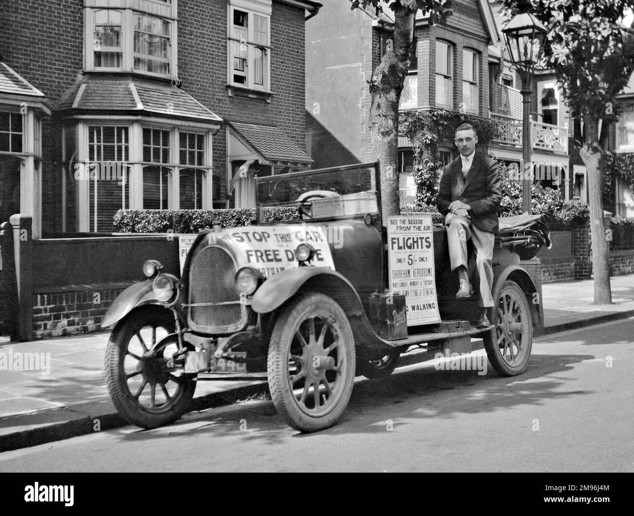 Advertising material displayed on a car, with a man sitting alongside.  One poster reads: Stop this car for a free drive, and the other reads: See the seaside from the air, flights only five shillings, Shoreham Aerodrome, Whit Sunday, Monday and Tuesday. Stock Photo