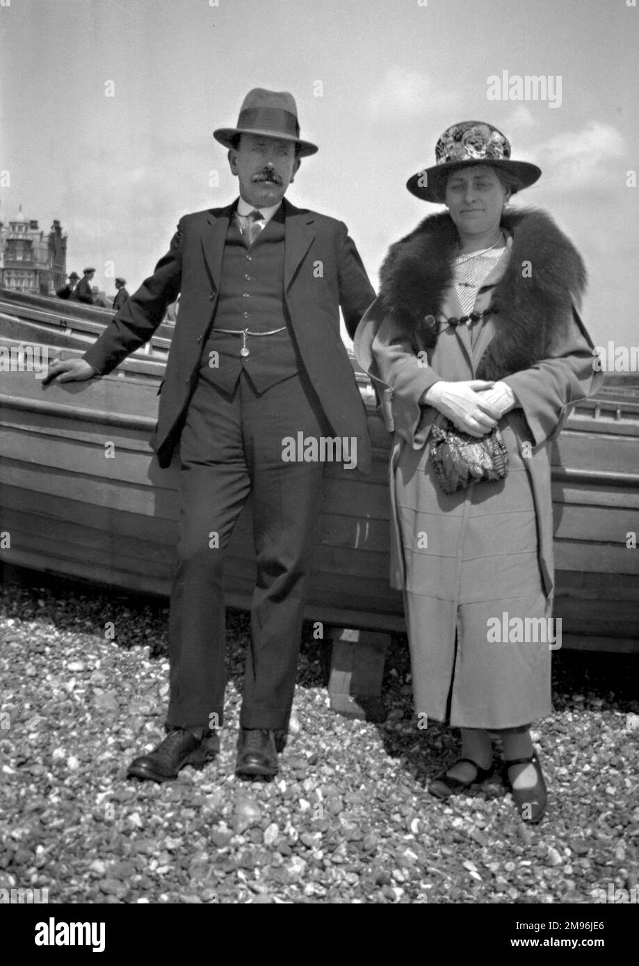 A middle-aged couple standing in front of some boats on a pebbly beach. Stock Photo