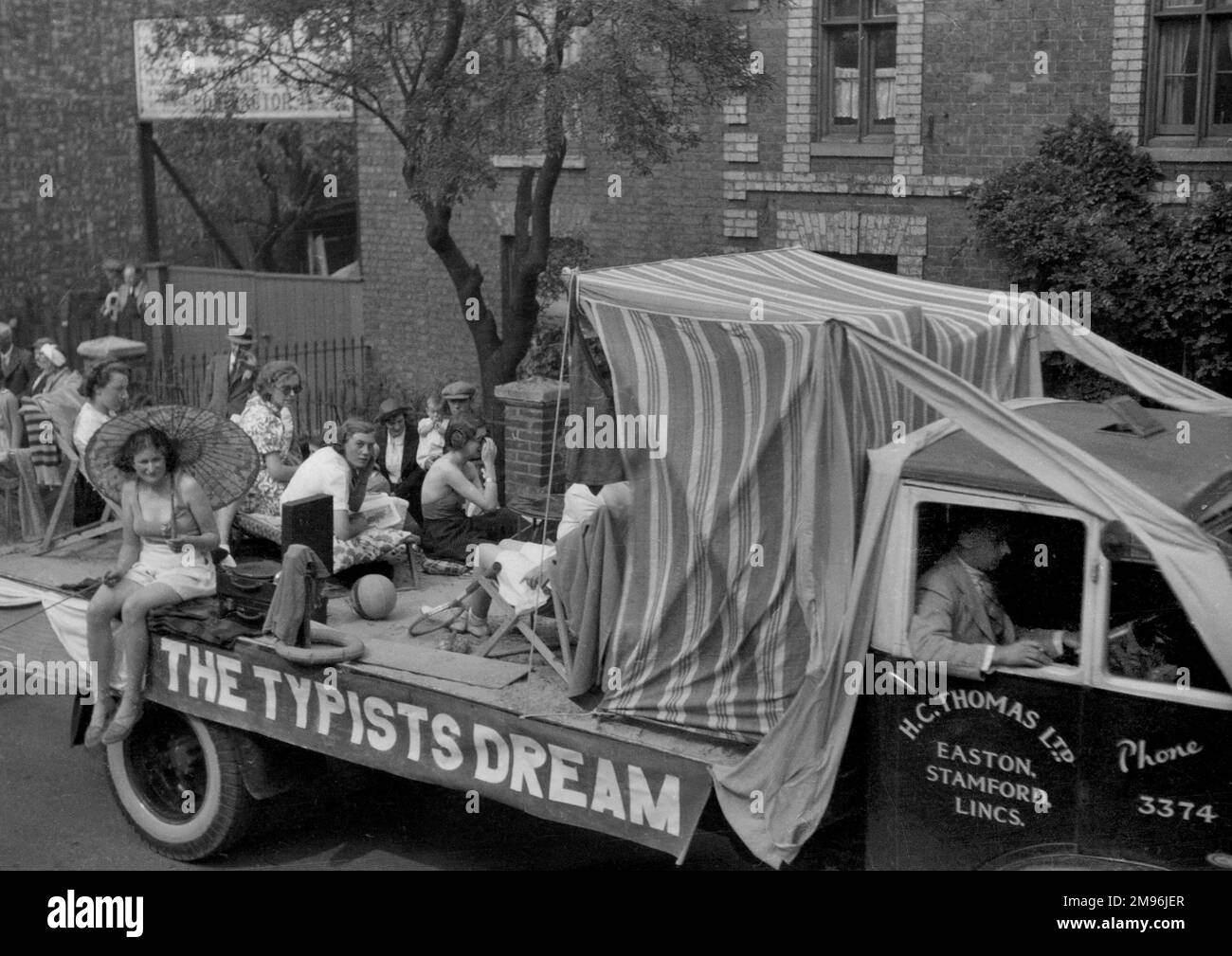 Carnival float, The Typist's Dream, showing young women in holiday attire, as if on a beach, rather than sitting in an office typing.  The van pulling the float belongs to H C Thomas Ltd of Easton, Stamford, Lincolnshire. Stock Photo