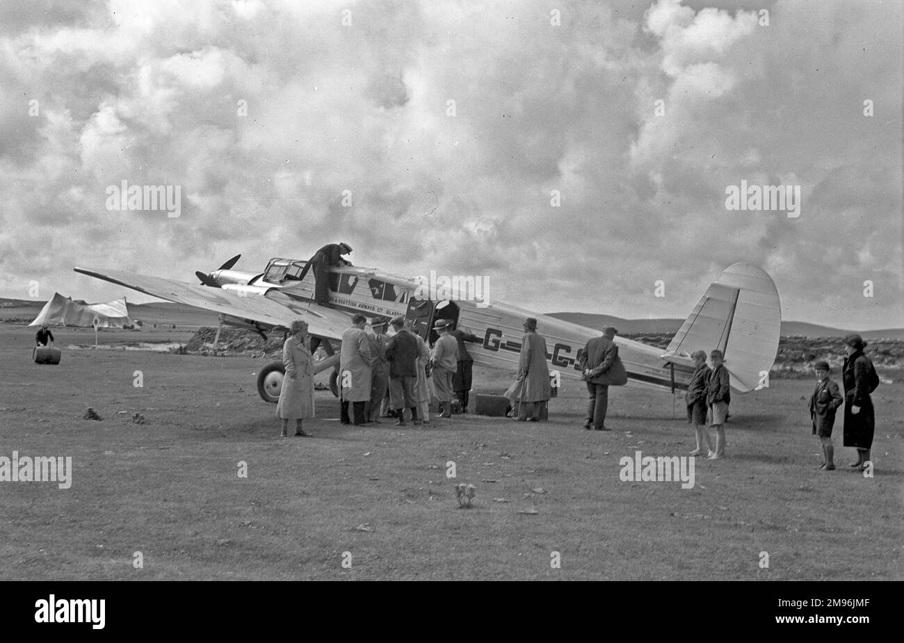 People on an airfield in Scotland with a light aircraft belonging to Northern & Scottish Airways Ltd of Glasgow. The G-ACSM was a Spartan Cruiser with three engines. Stock Photo