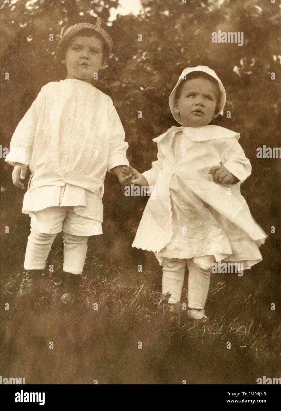A young brother and sister hold hands as they wander in the garden. Stock Photo
