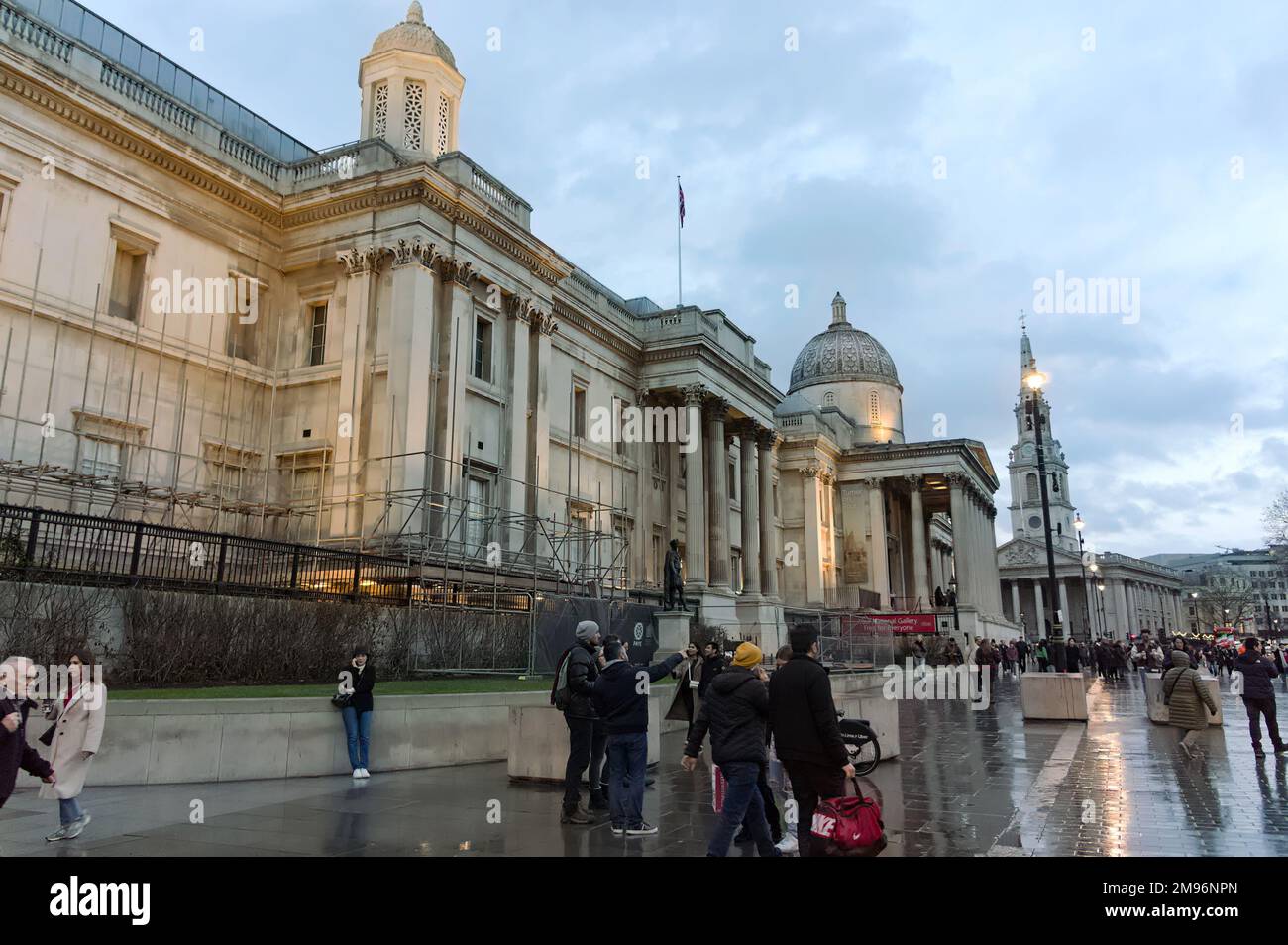 The National Gallery illuminated at sundown with people walking by on Trafalgar Square, Stock Photo