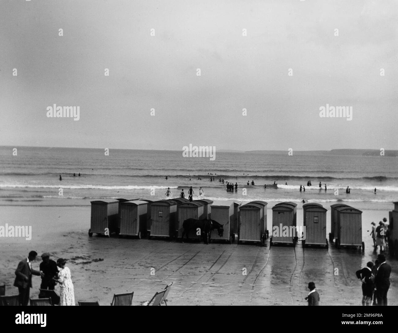 Bathing huts with wheels on the beach at Newquay, Cornwall, with a few holidaymakers. Stock Photo