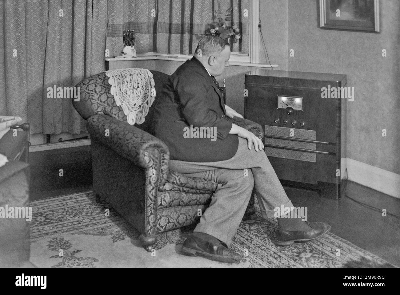 Man sitting in an armchair, listening to a large radio. Stock Photo