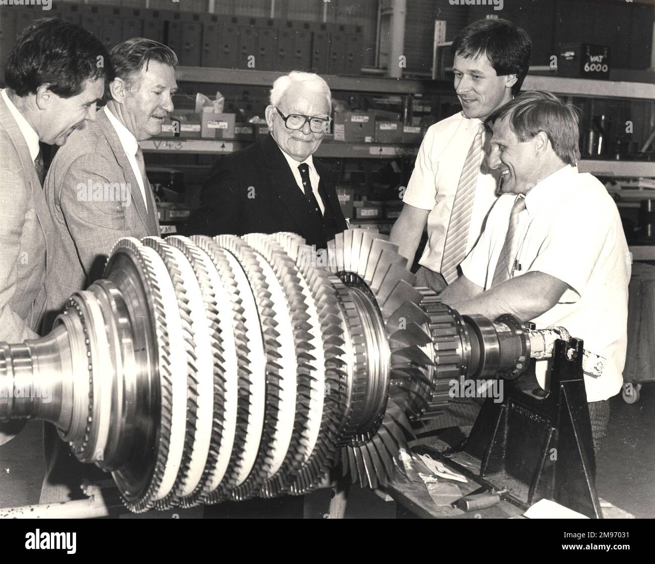 “Sir Frank Whittle (centre) the jet engine pioneer whose first engine ran successfully 50 years ago saw one of its direct descendants, the V2500 turbofan, at Rolls-Royce, Derby. The V2500 is 18 times more powerful than the first Whittle unit (WU) but uses less than one third as much fuel per pound of thrust. Here Sir Frank views the assembly of the high pressure compressor rotor. The first WU ran on 12 April 1937 at Whittle’s Power Jets company at Lutterworth only 35 miles from where Rolls-Royce’s Derby plant now stands.” 13 August 1987. Stock Photo