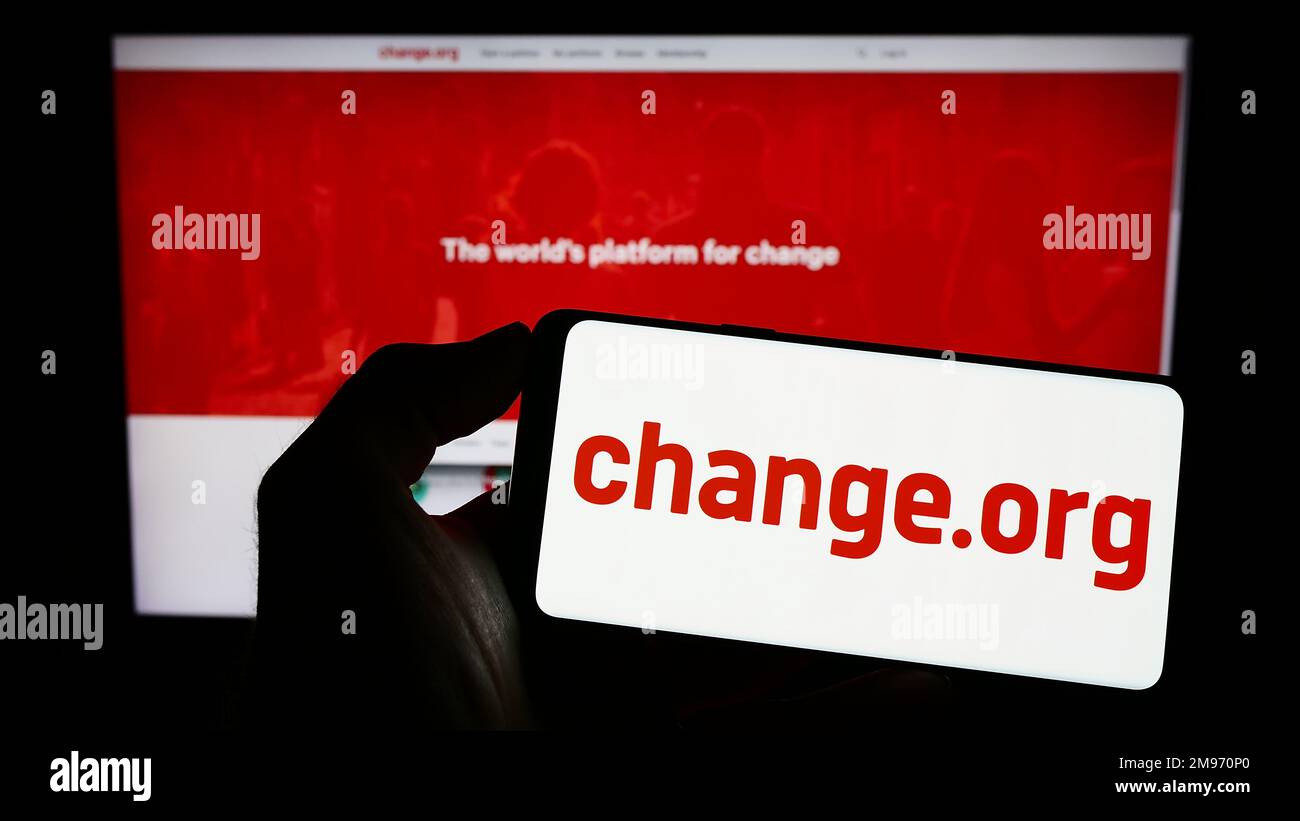 Person holding cellphone with logo of US petition platform Change.org PBC on screen in front of webpage. Focus on phone display. Stock Photo