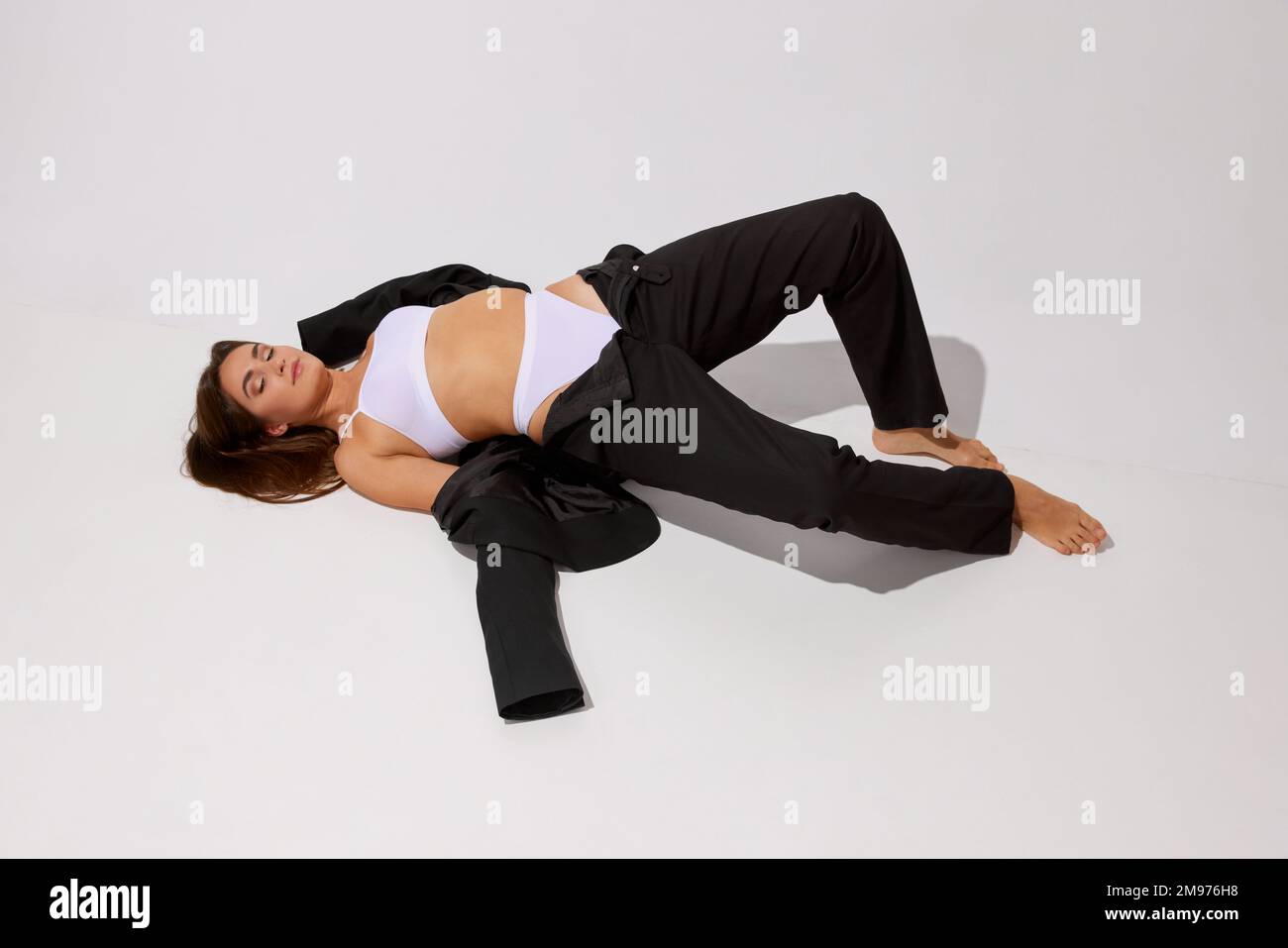Portrait of young fit girl posing in white underwear and black classic suit over grey studio background. Concept of body and skin care, fitness Stock Photo