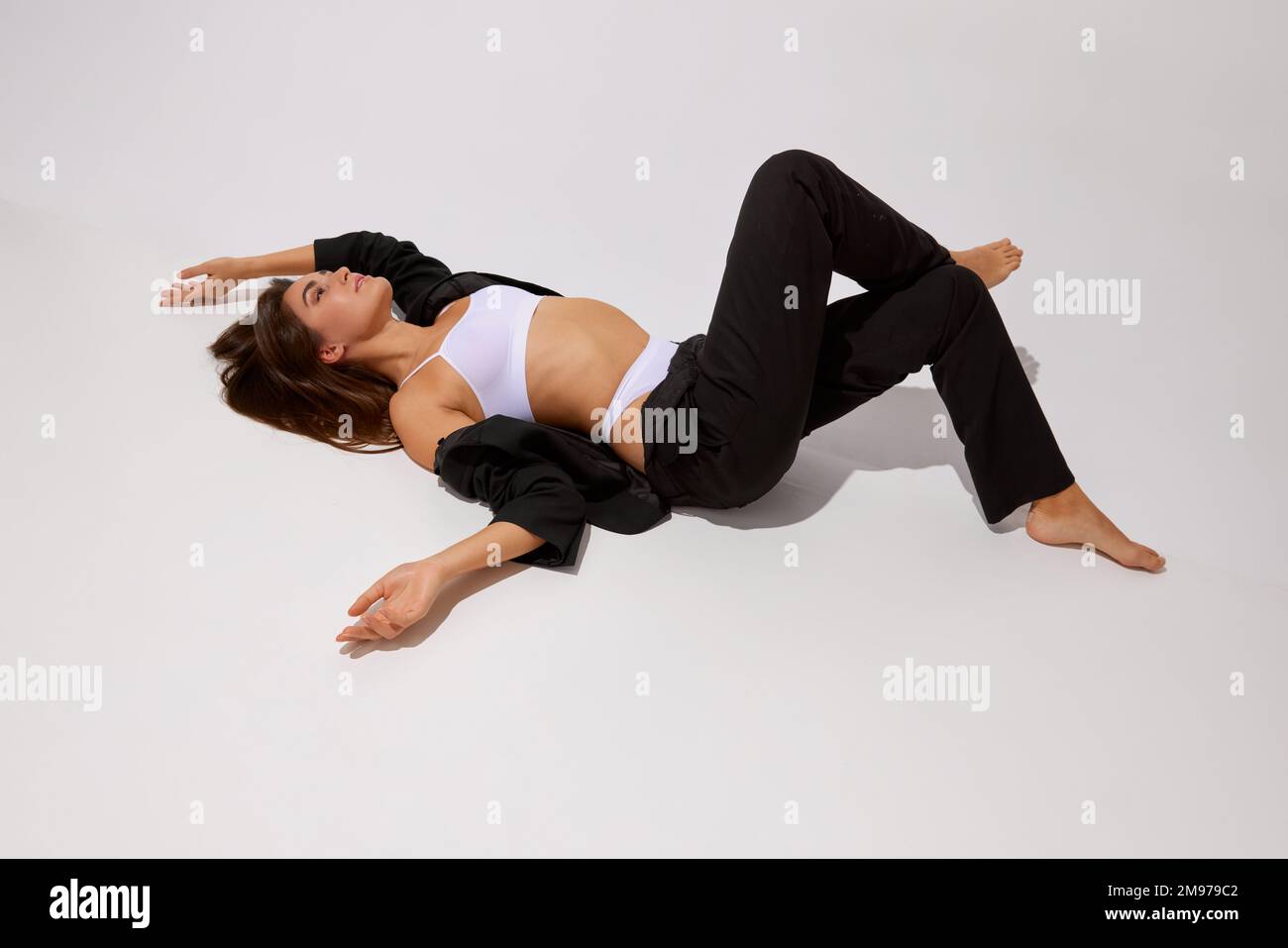 Comfy. Young beautiful girl posing in underwear and black classic suit over grey studio background. Concept of body and skin care, fitness Stock Photo