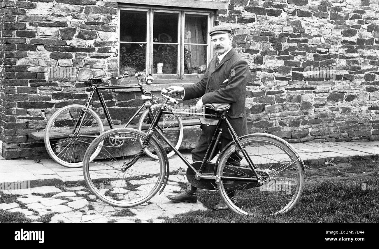 Man with bicycles outside house, known to be near Adlington in North East Cheshire. The bicycles would not look significantly out of place today. Notice te two female occupants of the house looking at the photography going on outside. Stock Photo