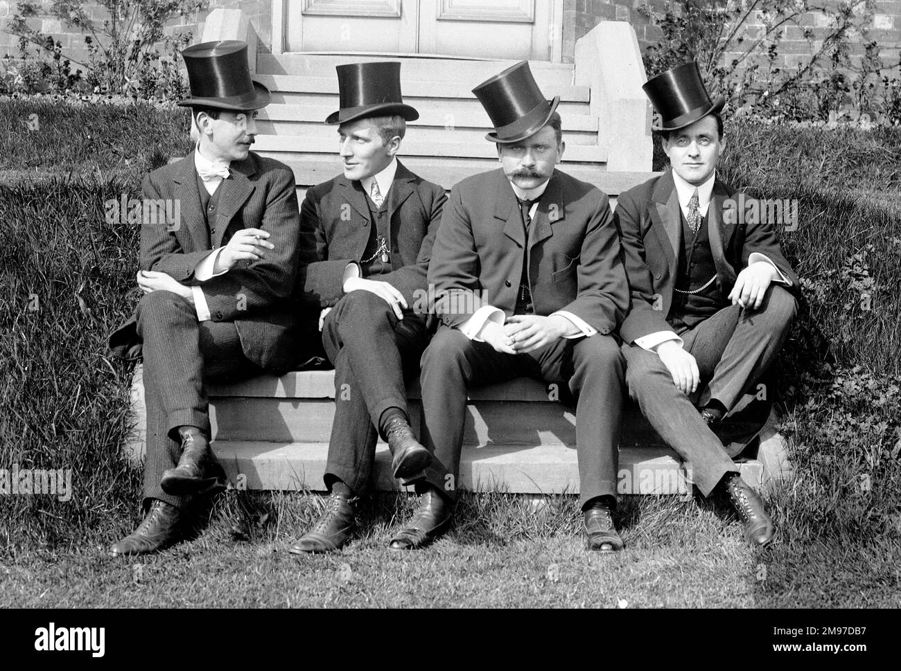Four well dressed Edwardian men named by the photographer - on the left is Ernest Battersby, the photographer, and their left is his brother James Johnson Battersby. The other two are named as Forster and Dickenson. They are sitting on the steps of the Battersby family home in Stockport, and their dress will reflect their upper-middle class status at the time. Stock Photo