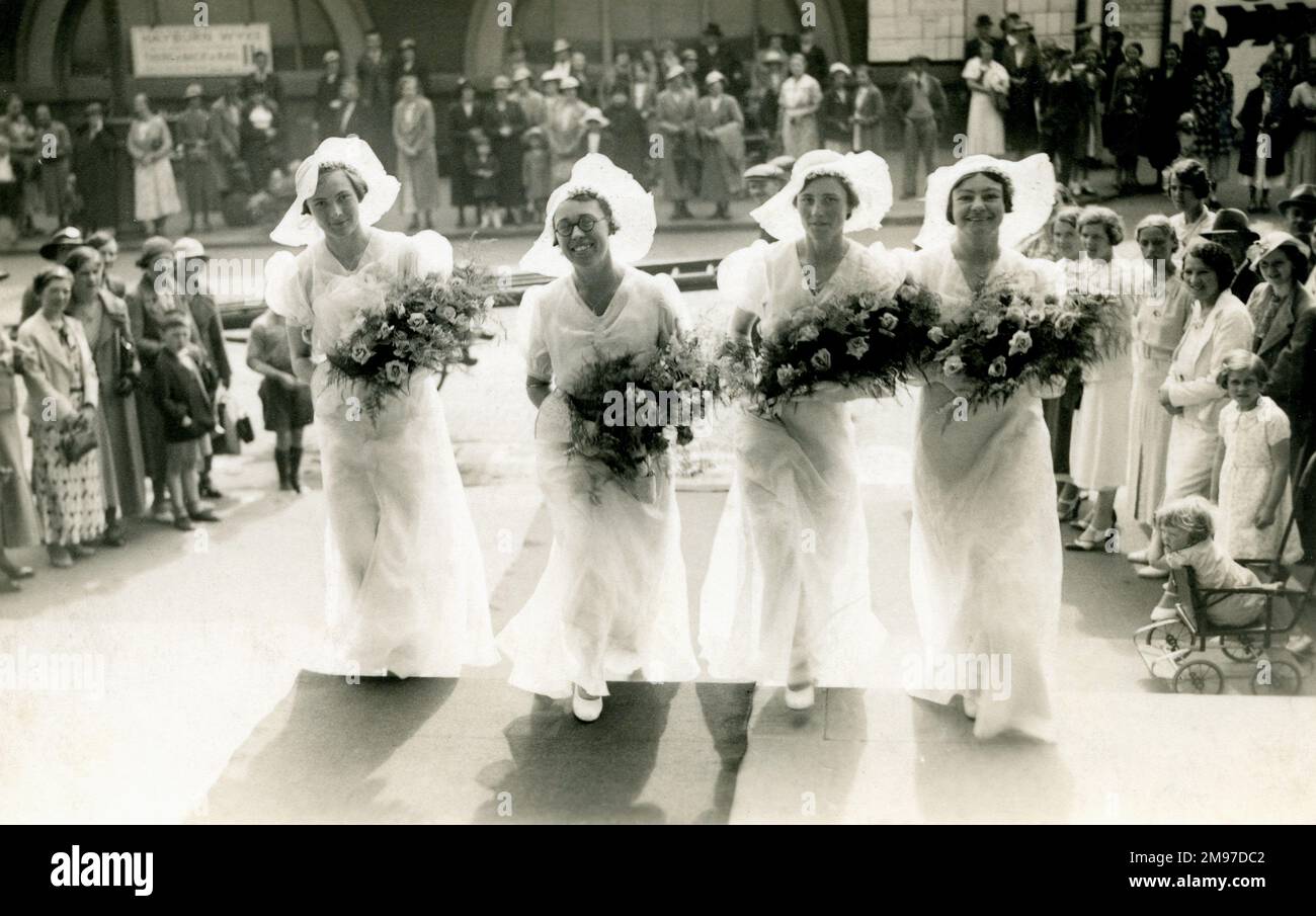 Wonderful photograph of four bridesmaids arriving at a society wedding dressed in long flowing gowns and wide-brimmed hats, and carrying huge bouquets of flowers. Stock Photo