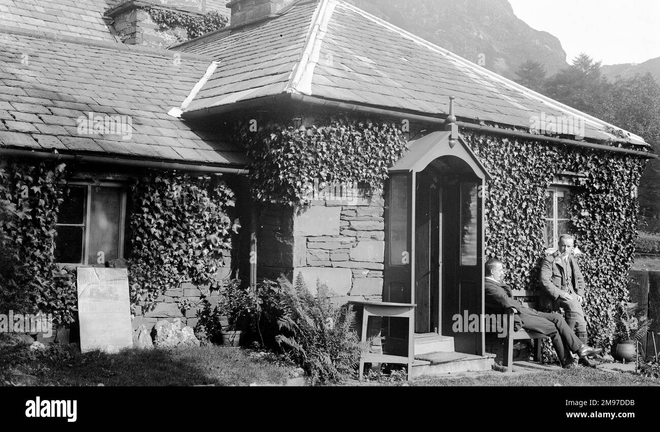 Ivy Cottage, near Coniston in the Lake District may well still exist but its exact location is uncertain. Ernest Battersby's friends Wilson and Nelstrop are outside the door, and a sign to the left of the door advertises 'Coach Tours from Coniston', courtesy of W J Baines, Black Bull Hotel Coniston - an establishment still going today. Stock Photo