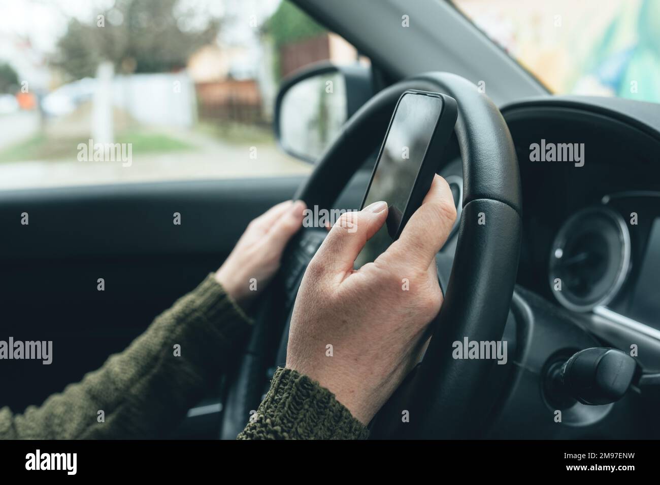 Closeup shot of female hand typing message on smartphone device, casual woman driver wearing green knitted sweater using mobile phone in vehicle inter Stock Photo