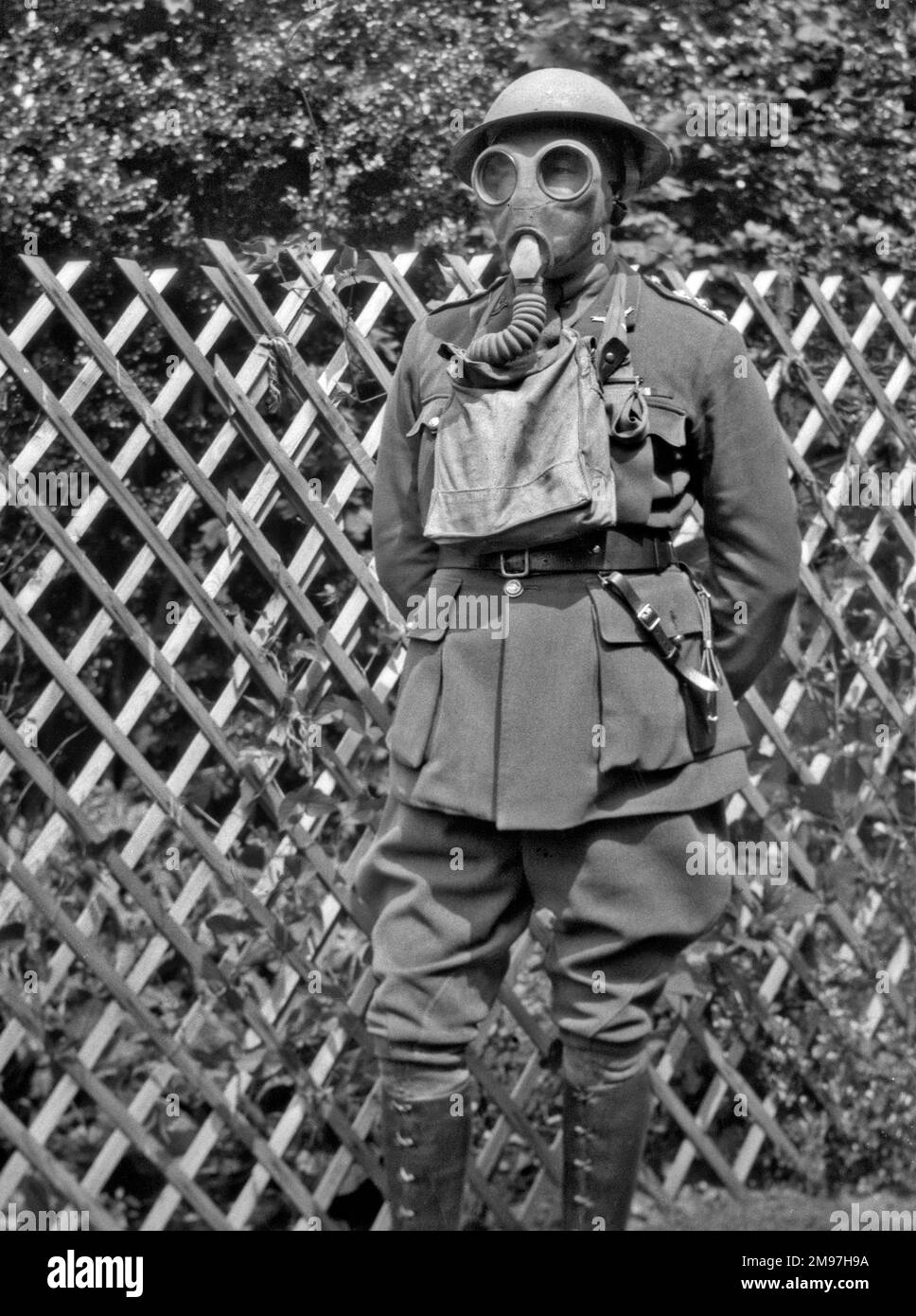 Man in uniform, tin helmet and gas mask, posing in a garden, probably during the Second World War. Stock Photo