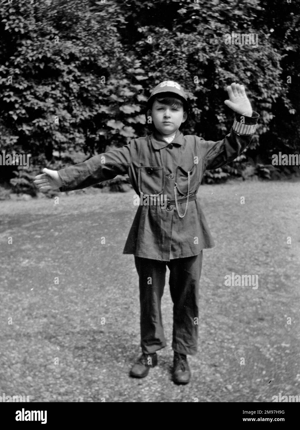 Boy in policeman's uniform in a garden, pretending to direct traffic. Stock Photo