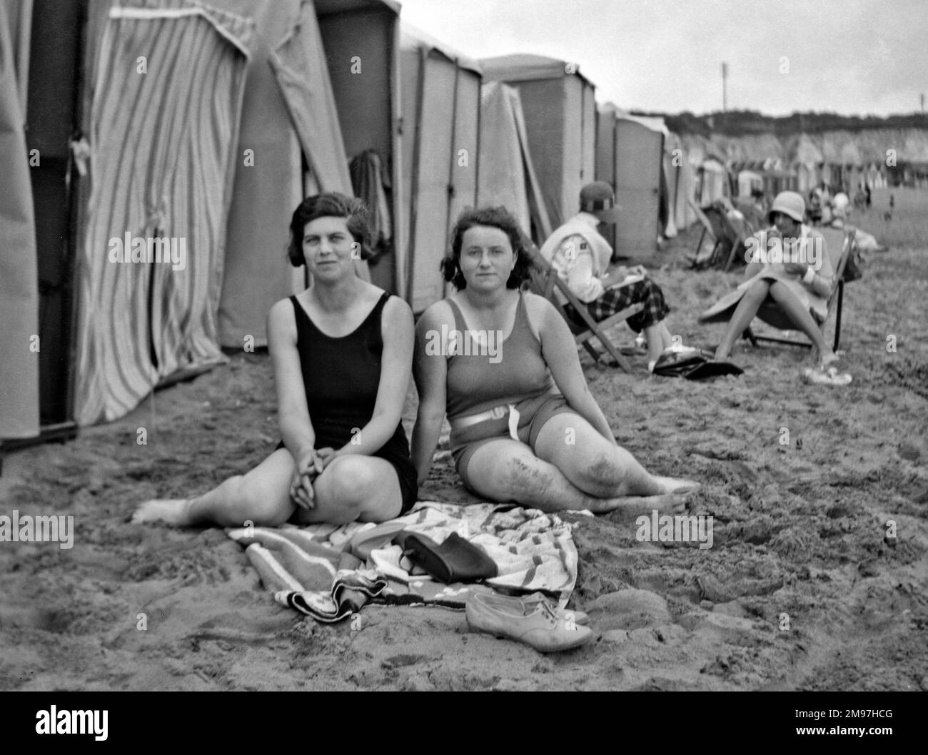 Women sitting on a beach at a seaside resort with a row of bathing tents nearby. Stock Photo