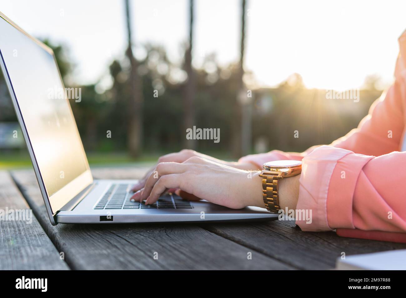 Unrecognizable person at a wooden table in a park using his laptop outdoors. Stock Photo