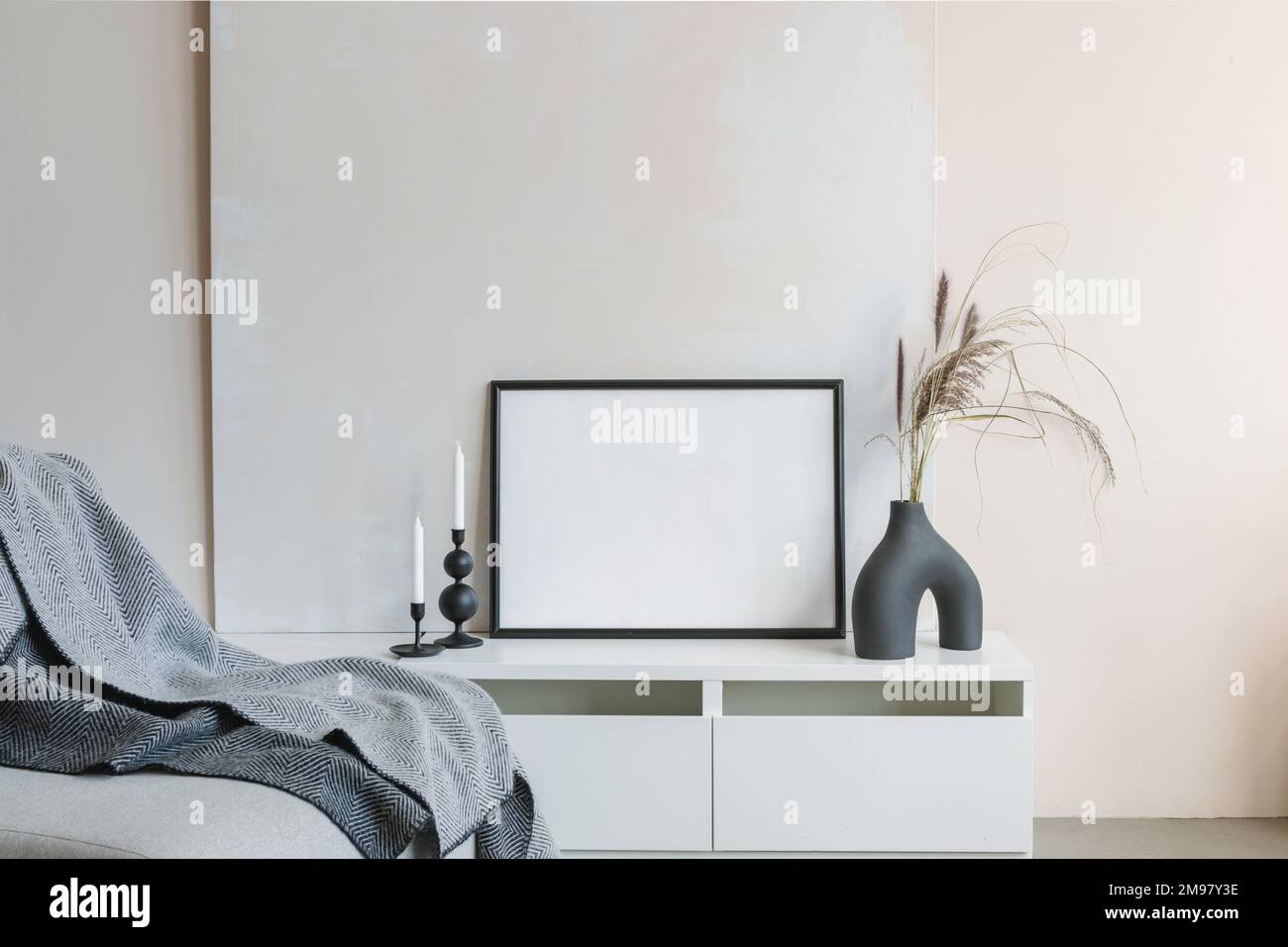 Modern ceramic vase with two candlesticks and an empty picture frame on a sideboard next to a sofa Stock Photo