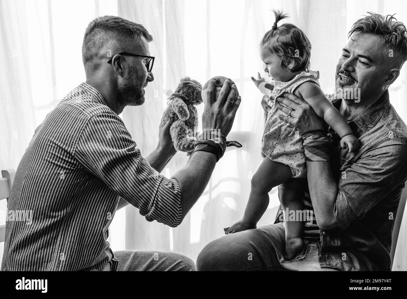 Male gay couple with adopted baby girl at home - Two handsome fathers playing with their daughter - Lgbtq+ family at home - Diversity concept and LGBT Stock Photo