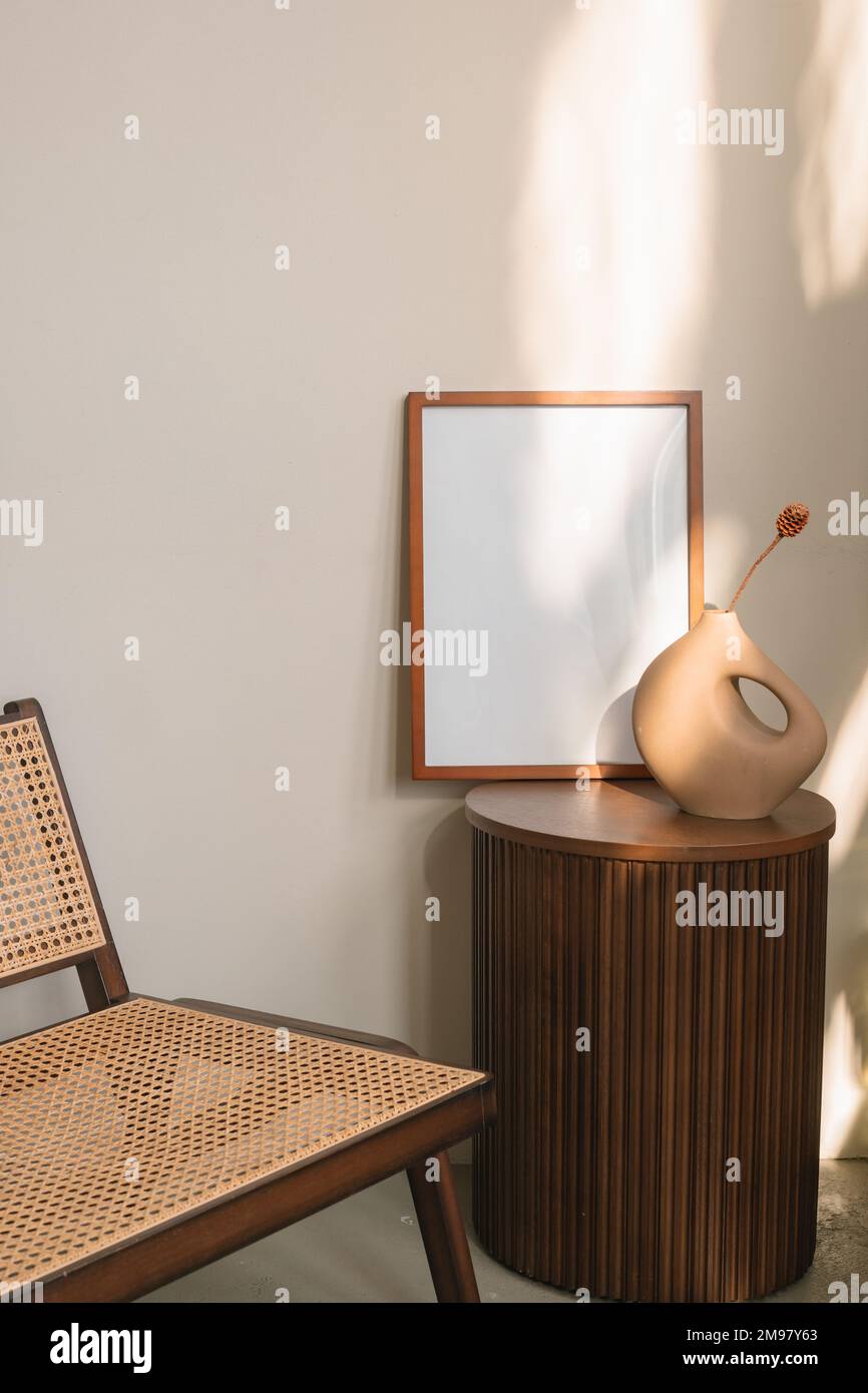 Blank wooden picture frame and modern vase on a side table next to a chair Stock Photo