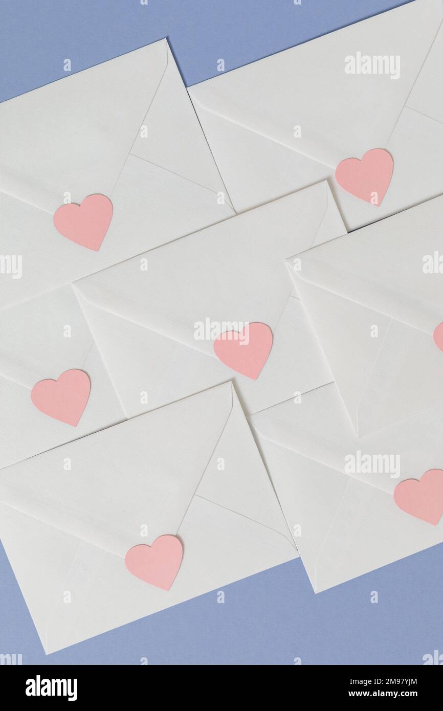 Overhead view of assorted pastel coloured envelopes and heart shaped stickers on a blue background Stock Photo