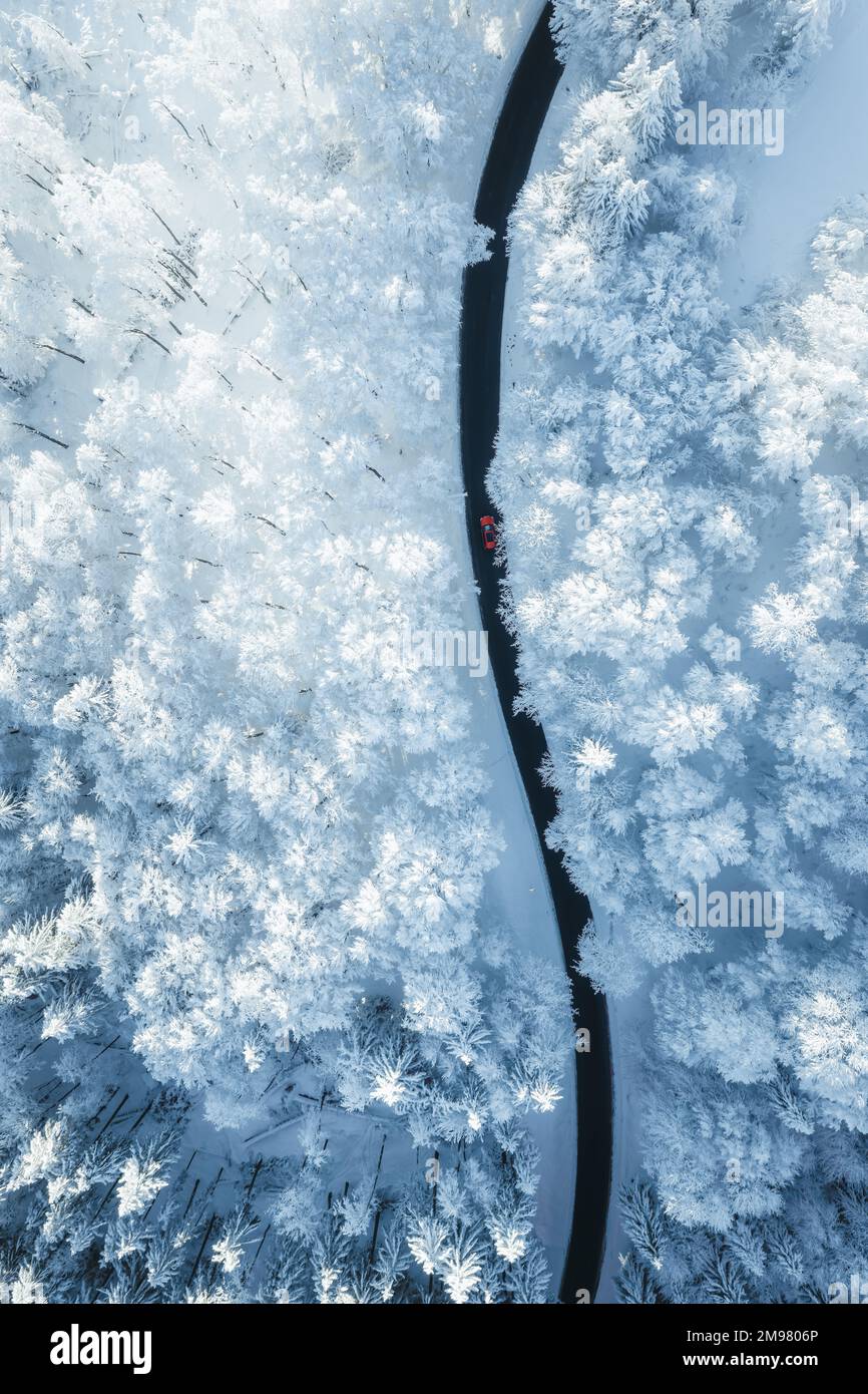 Aerial view of a car driving on a road through a snowy forest in winter, Salzburg, Austria Stock Photo