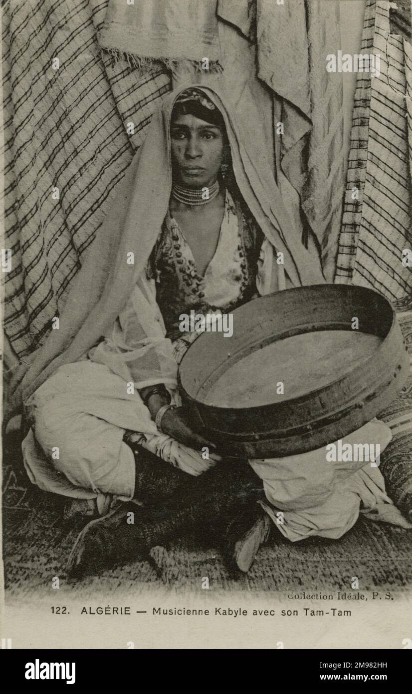 A female Kabyle musician sits cross-legged holding her Tam-Tam (a type of  gong). The Kabyle are a Berber ethnic group originating from Kabilya in Northern Algeria. Stock Photo