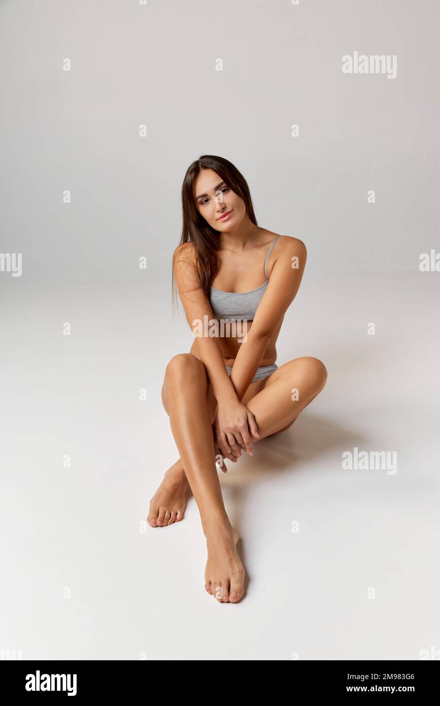 Portrait of young beautiful girl with brunette long hair posing in underwear over grey studio background. Concept of body and skin care, fitness Stock Photo