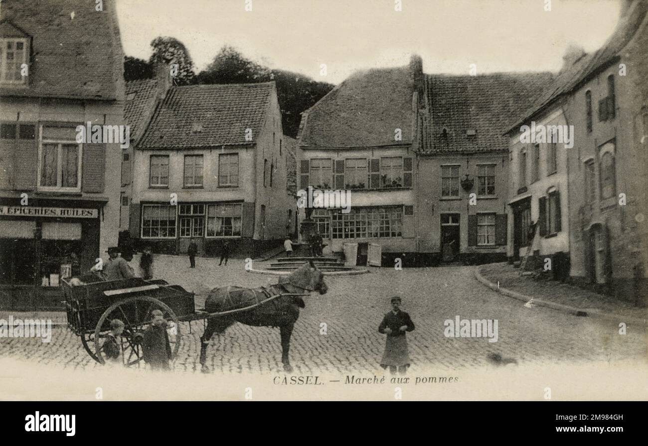 Cassel, France -- a horse and cart stand with townspeople and children at the Marche aux pommes (apple market) town square, with houses and a statue visible in the background. Stock Photo